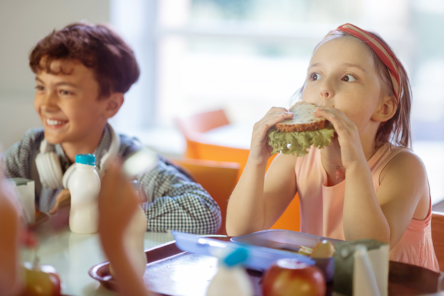 Schüler sitzen gemeinsam am Tisch und essen ihr Mittagessen im Schulbistro